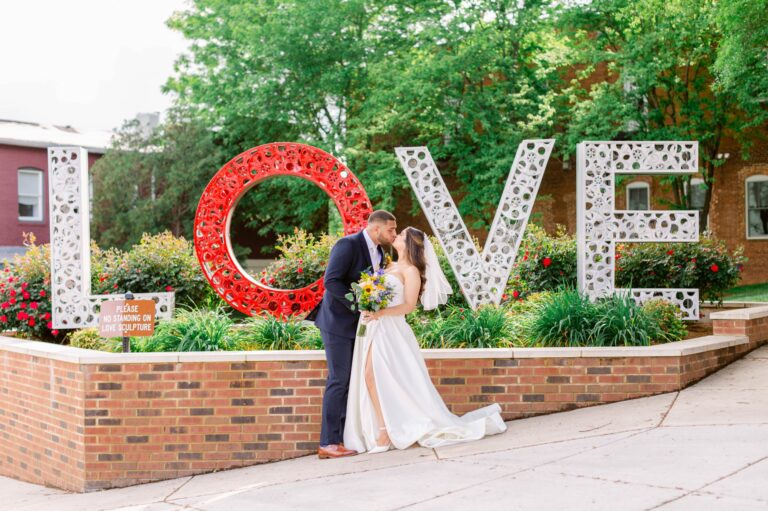 A bride and groom kiss in front of a large, decorative 