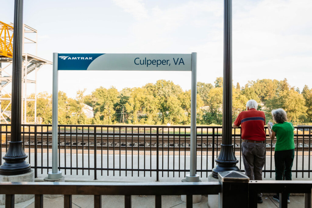 two people standing at an Amtrak platform with a sign that reads Culpeper