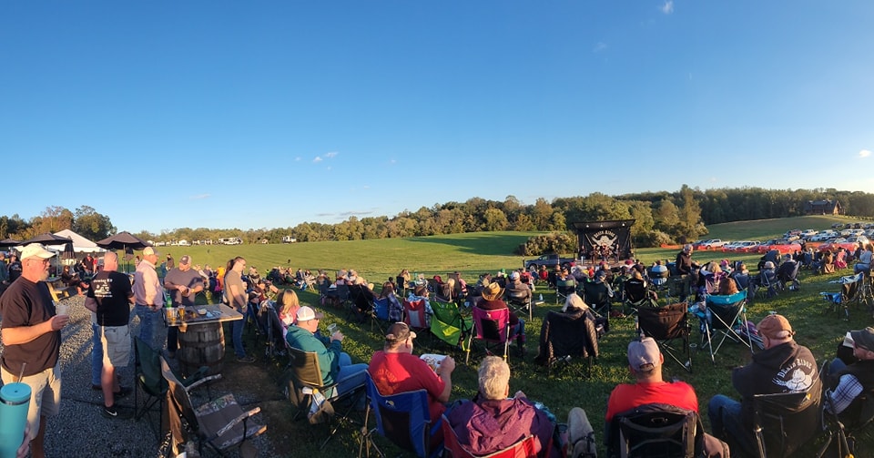 large crowd of people outside in a field with a stage in the background